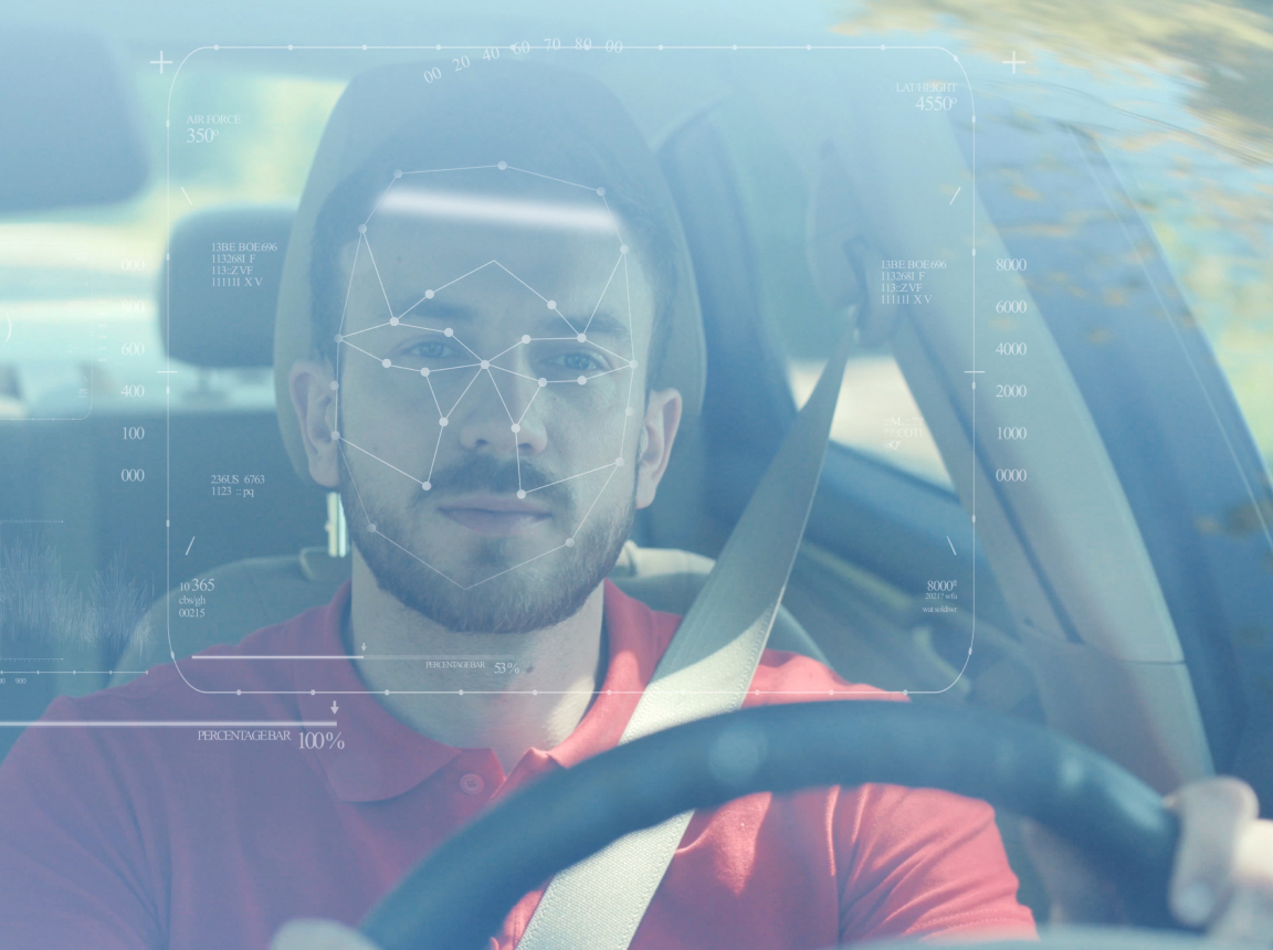 A view through the windshield of a driver at the wheel, with biometric technology scanning his face
